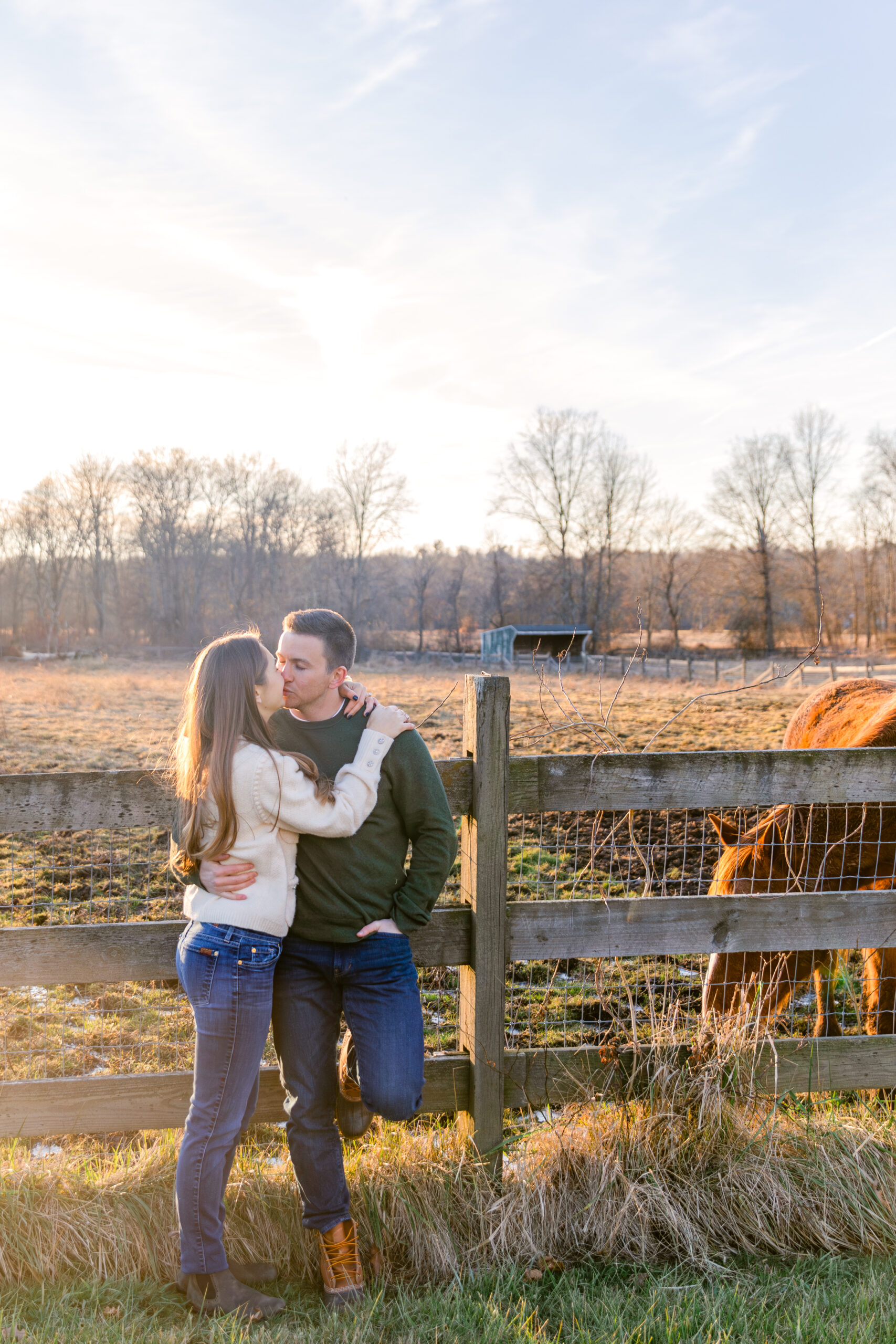 Couple leaning on a fence with a horse on a farm